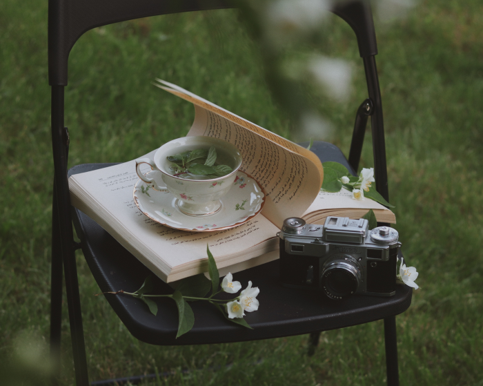 Book on a chair with a cup of tea and an old camera alongside the book.