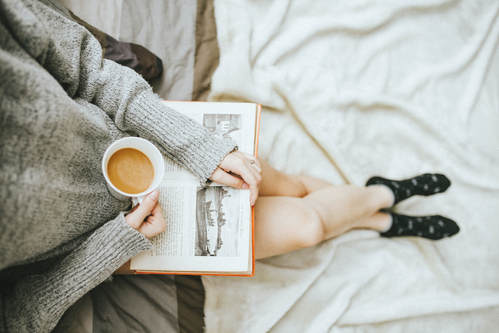 Woman holding a coffee and reading a book.