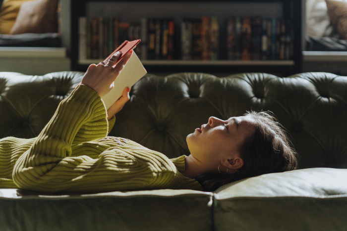 Beautiful woman lying down on a couch and reading a book.