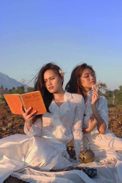 Two beautiful asian girls wearing white dresses and reading Mark Twain.