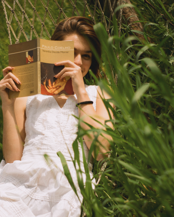 Beautiful girl wearing a white dress reading a book in the grass. book blog list and book blogger list (Flyintobooks.com)