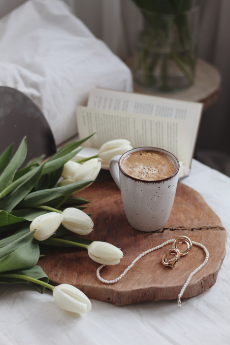 White tulips with a coffee on a bed.