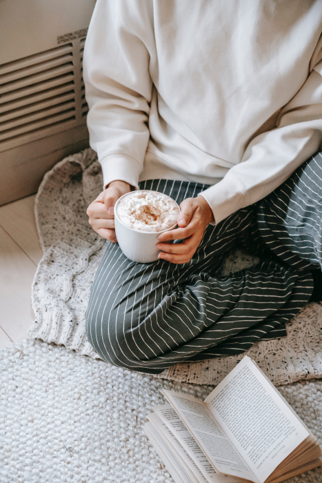 Girl wearing striped pants reading a book and holding a coffee. book blog list and book blogger list (Flyintobooks.com).