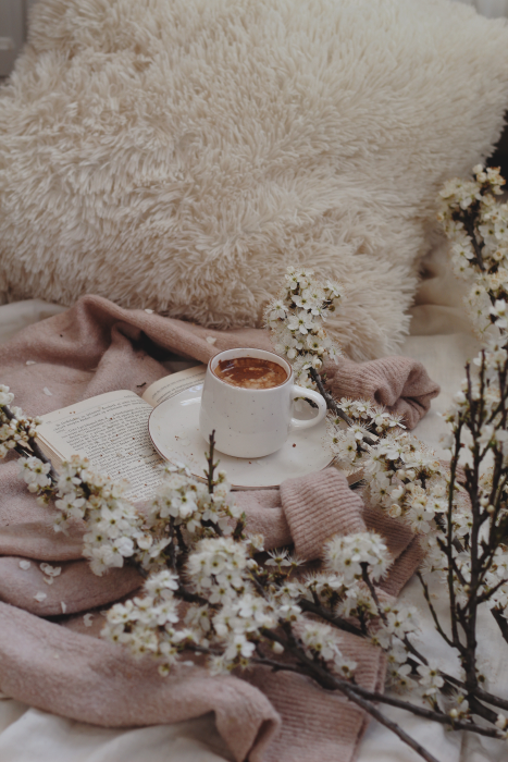 Book open with a white coffee cup and saucer on top of a beige sweater.